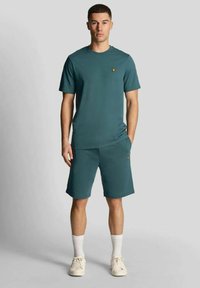 Completo t-shirt e pantaloncini turchese, realizzato in tessuto morbido. Caratteristiche: scollo rotondo, maniche corte e logo ricamato sul petto. Scarpe da ginnastica bianche e calzini.