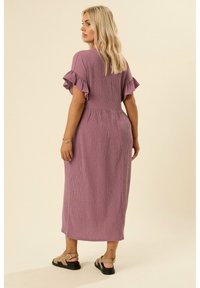 Abito lungo in tessuto viola chiaro colorato con maniche a frangia corte e vita aderente, indossato con sandali flat.