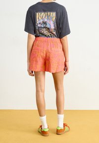 Svart grafisk t-shirt med palmträdsmotiv, i kombination med rosa mönstrade shorts med fickor. Bärs med färgglada sneakers och vita strumpor.