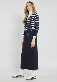 Granatowy i kremowy kardigan w paski noszony na białym golfie, w zestawieniu z długą granatową spódnicą i białymi sneakersami z czarnymi akcentami.