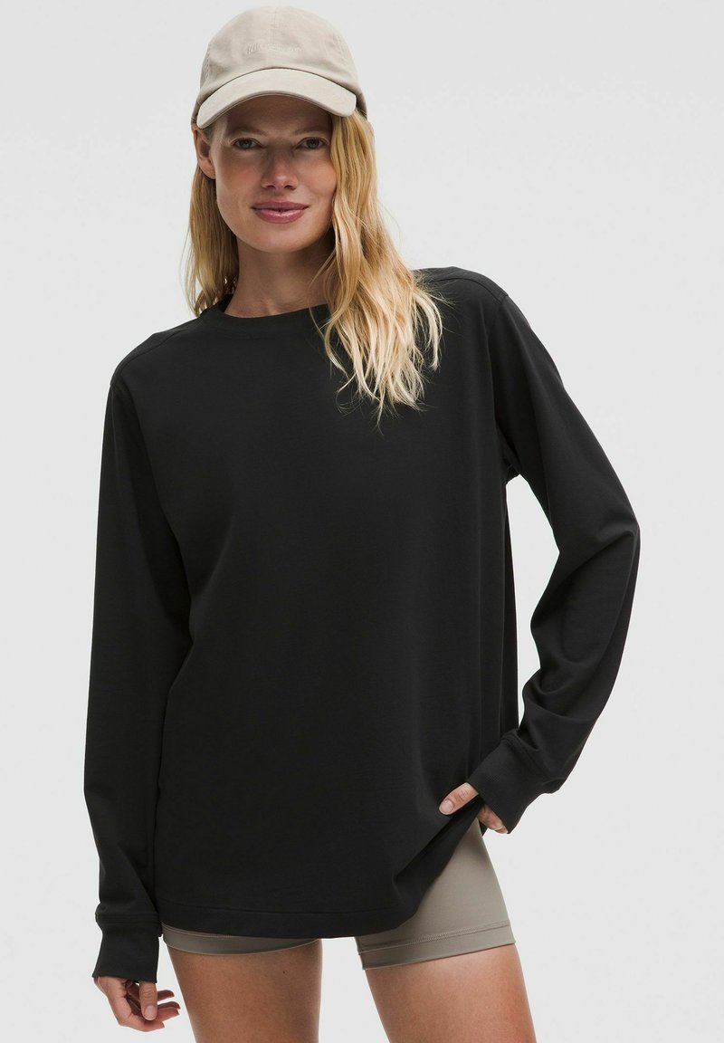 Chemise noire à manches longues avec un col rond et une coupe décontractée. Associée à un short couleur peau. Présente une texture douce et des manches longues.