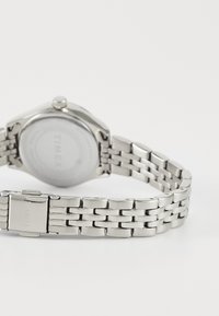 Silver stainless steel watch with a round case and a linked bracelet. The back displays a smooth surface with the brand name "TIMEX."