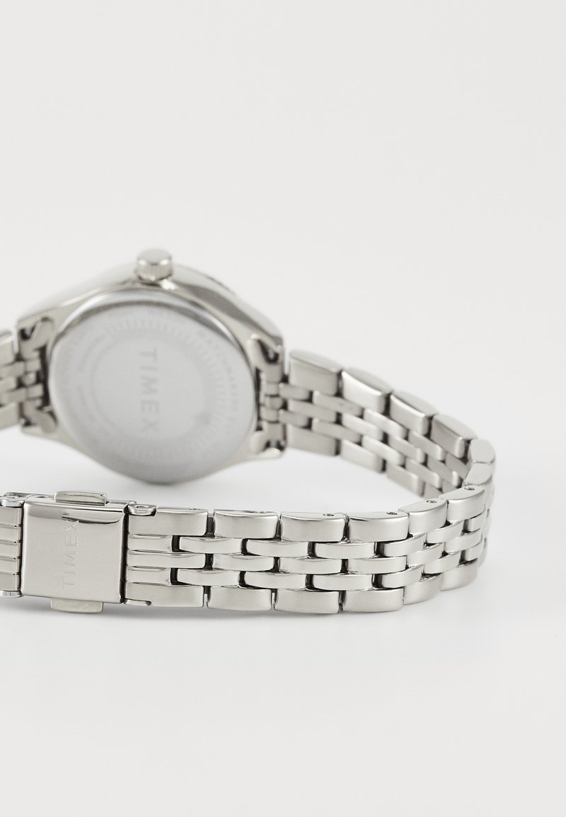 Silver stainless steel watch with a round case and a linked bracelet. The back displays a smooth surface with the brand name "TIMEX."