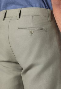 Khaki trousers made of lightweight fabric, featuring a flat back pocket with a button and belt loops at the waist.