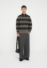 Dark gray striped sweater with a round neckline, worn over a black collared shirt. Loose gray pinstriped trousers and a black crossbody bag.