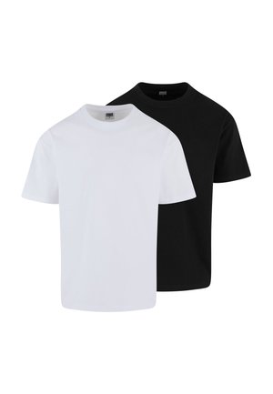 Jeune homme aux cheveux courts portant un t-shirt blanc uni et un jean bleu clair sur un fond gris clair.