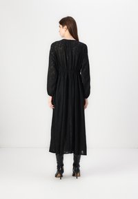 Μαύρο φόρεμα με μακριά μανίκια, με καθορισμένη μέση και διάφανη υφή. Φορεμένο με μαύρες μποτες ως το γόνατο.