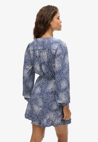 Vestido azul con patrón de puntos blancos, mangas largas abullonadas, cintura ajustada, dobladillo con volantes, hecho de una tela liviana, adecuado para uso casual.