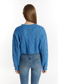 Pulover bleu tricotat cu un model de cablu, design scurt și mâneci lungi. Purtați cu blugi cu talie înaltă, evidențiind detalii tricotate texturate.