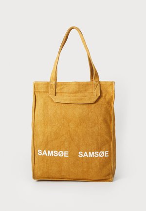 Žlutá taška přes rameno vyrobená z měkkého materiálu, s dvěma uchy a bílým nápisem "SAMØE SAMØE" na přední straně. Obdélníkový tvar s texturovaným povrchem.