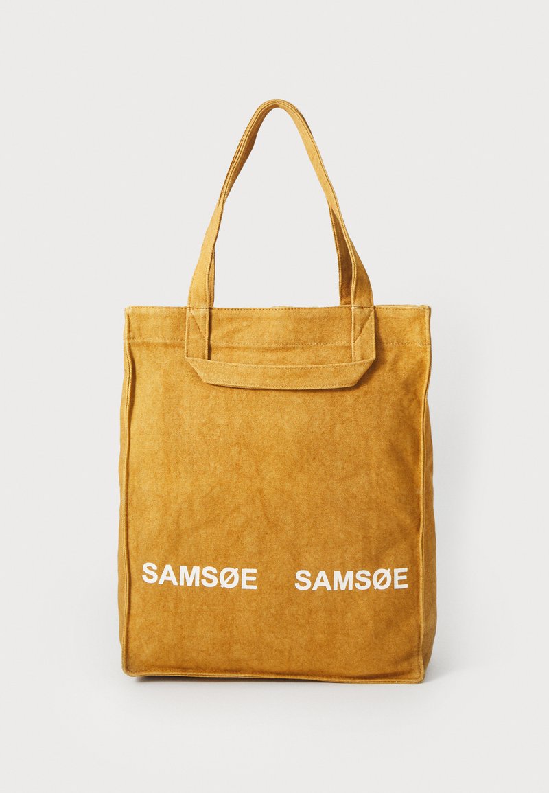 Gul tote-veske laget av mykt materiale med to håndtak og hvit tekst "SAMØE SAMØE" på forsiden. Rektangulær form med en linjete tekstur.