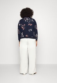 Maglione blu marina con motivo floreale in rosa e bianco, dotato di polsini a coste. Abbinato a pantaloni bianchi larghi, in tessuto liscio e vestibilità ampia.