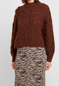 Brown knitted sweater with a chunky cable pattern and a high neckline, paired with a patterned pencil skirt in beige and black.