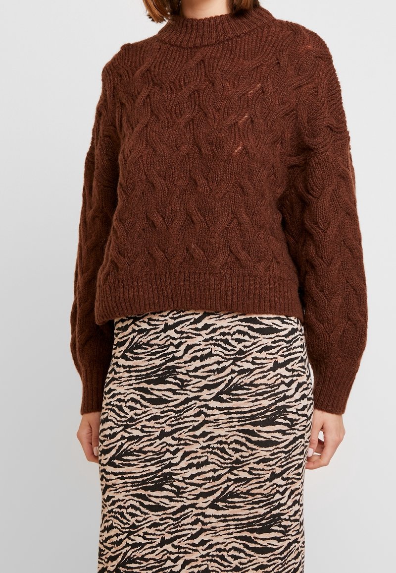 Brown knitted sweater with a chunky cable pattern and a high neckline, paired with a patterned pencil skirt in beige and black.