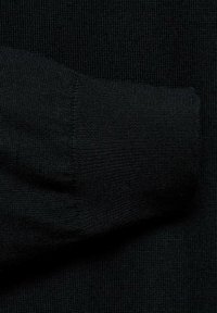 Gros plan sur un tissu de pull en laine noir tricoté, mettant en valeur une texture côtelée et un poignet replié, avec une surface lisse et uniforme.