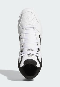 White sneaker with black accents, smooth leather upper, perforated toe box, laces, and branded tongue featuring a basketball motif.