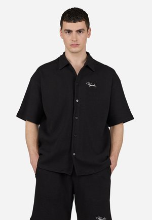 Black short-sleeve shirt featuring a button-up front, pointed collar, and textured fabric. White logo accent on the left chest area.