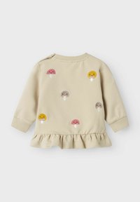 Sweatshirt crème avec ourlet à volants, orné de champignons brodés colorés en rose, jaune et gris. Poignets et encolure côtelés.