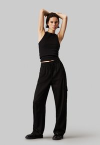 Sort ribbet trøje uden ærmer, der er parret med løse sorte cargo bukser med elastisk talje og sidelommer. Skinnende sorte sko.