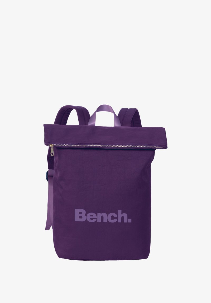 Sac à dos violet avec un design à rabat, fermeture éclair et grand logo "Bench". Fabriqué en tissu tissé avec des sangles réglables et une poignée supérieure.