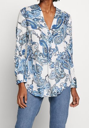 Hvid langærmet bluse med blå paisley blomsterprint, båret med lyseblå jeans, med dyb V-hals og knapmanchetter.