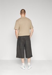 Camiseta de algodón beige de manga corta, combinada con pantalones cortos de mezclilla negros de corte holgado y dobladillo deshilachado, llevada con zapatillas blancas.