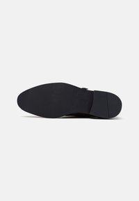 Semelle de chaussure en cuir noir avec une surface texturée, une forme légèrement courbée et un détail de logo. La semelle est plate avec des rainures de traction minimales.