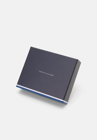 Námornícky modrá obdélníková krabice s lesklým povrchem, která má bílý logo "TOMMY HILFIGER" a tenký pruhovaný akcent v červené, bílé a modré barvě na spodní části.