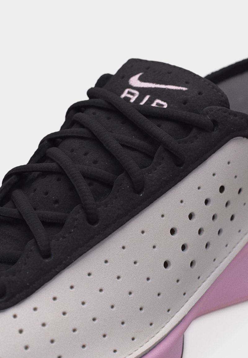 Close-up van een zwarte en grijze Nike Air sneaker met geperforeerde zijkant en lavendelkleurige zool, met de nadruk op de veters en het logo op de tong.