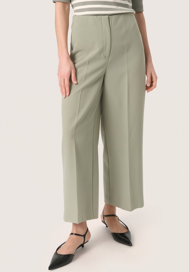 Lichtgroene wijde broek met hoge taille, met een gladde textuur en subtiele naden aan de zijkant, gecombineerd met zwarte puntige schoenen.