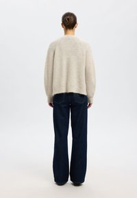 Jasnobeżowy sweter z dzianiny o luźnym kroju, z prążkowaną fakturą, opuszczonymi ramionami i surowym wykończeniem na dole. Połączony z szerokimi jeansami w ciemnym niebieskim kolorze.