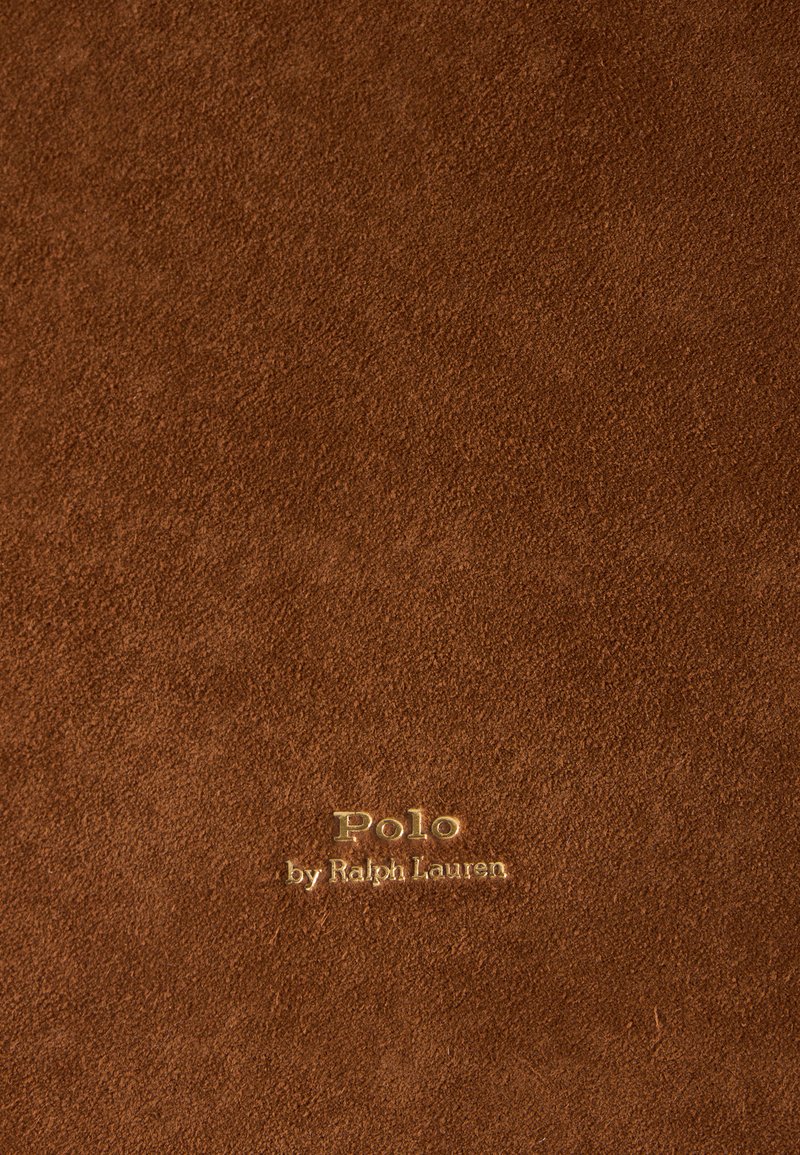 Texture en daim marron avec texte embossé doré « Polo by Ralph Lauren » centré sur la surface.