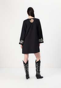 Μαύρο φόρεμα με μακριά μανίκια που διαθέτει διακοσμητική κεντητική στα μανίκια. Μαύρες καουμπόικες μπότε�ς με κομψό τακούνι και περίπλοκη ασημένια ραφή.