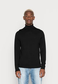 Maglione nero a collo alto realizzato in un tessuto morbido, con maniche lunghe e un design aderente. Abbinato a jeans strappati di colore blu chiaro.