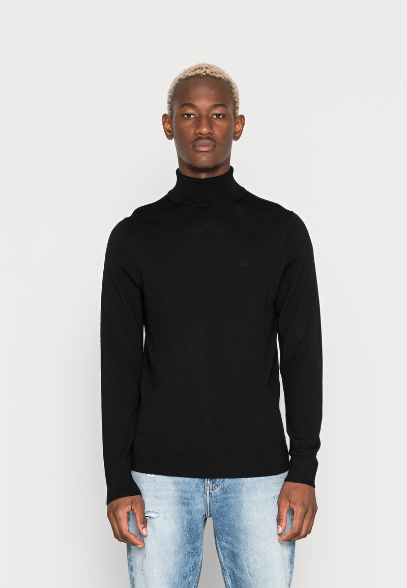 Maglione nero a collo alto realizzato in un tessuto morbido, con maniche lunghe e un design aderente. Abbinato a jeans strappati di colore blu chiaro.