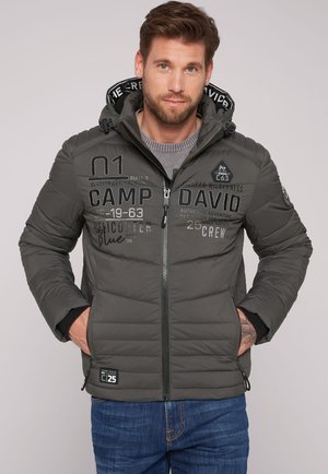 Chaqueta acolchada gris con cremallera frontal, puños elásticos y gran texto impreso en el pecho. Cuenta con una capucha con forro estampado y bolsillos.