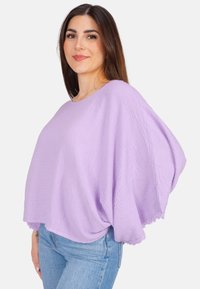 Lavendel Batwing-Top aus strukturiertem Stoff, mit rundem Ausschnitt und Spitze am Saum, kombiniert mit hellblauen Jeans.