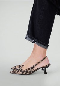 Feet wearing black and brown leopard print slingback kitten heels paired with black cuffed denim jeans.