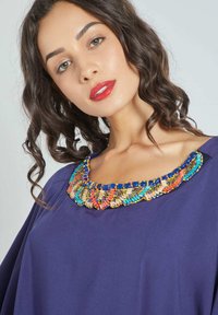 Prenda púrpura con un escote adornado con cuentas que presentan un patrón decorativo de cuentas multicolores. Textura suave, mangas anchas y cuello redondeado.