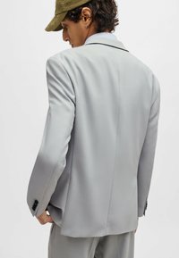 Light grey tailored blazer with structured shoulders, smooth texture, single vent, and three black buttons on each cuff.