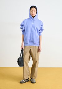 Felpa oversized viola chiaro, pantaloni cargo beige, borsa nera e scarpe nere con strisce bianche a zebra. Lo sfondo è di un colore chiaro uniforme.