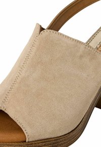 Beige ruskinds slingback sandal med åben tå, syet detaljer og en lav korkvedge. Glat tekstur og subtile åre er synlige.