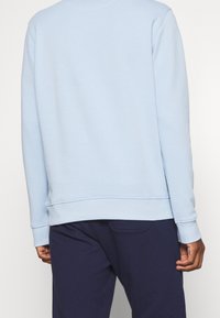 Světle modrá mikina s kulatým výstřihem, ribbovanými manžetami a lemem. Měkká, strukturovaná látka. V kombinaci s tmavě modrými kalhotami.