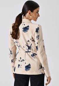 Floral blazer in zacht beige met marineblauwe en blauwe abstracte bloemen. Licht getailleerd ontwerp met een taille die is geaccentueerd en lange mouwen. Soepele stofstructuur.