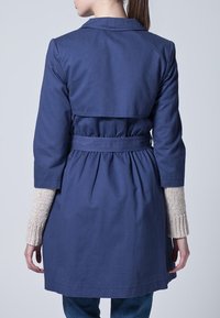 Granatowy płaszcz trench z paskiem w talii, posiadający długie rękawy z dzianinowymi jasnoszarymi mankietami oraz rozcięciem z tyłu.