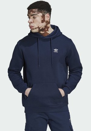 Felpa blu navy con tasca davanti, cappuccio con cordino e logo bianco Adidas sul lato sinistro del petto. Realizzata in un tessuto morbido.