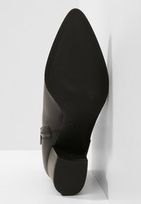 Schwarzer Leder-Pumps mit spitzer Zehe. Verfügt über ein glattes Obermaterial, eine strukturierte Gummisohle und einen dekorativen seitlichen Riemen.