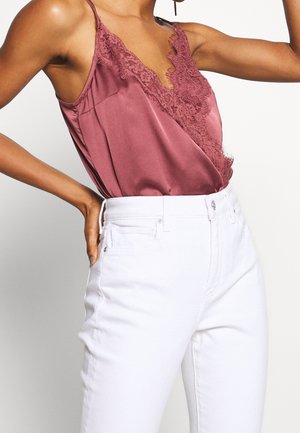 Satin camisole i støvet rosa med blondekant langs udskæringen, parret med højtaljede hvide jeans. Glat tekstur og delikate detaljer.