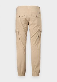 Beežid tööpüksid nööpidega tagataskutega, külgfläpp-taskutega, õmmeldud põlvedetailidega ja elastsete varrukaäärtega.