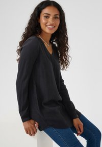 Long-sleeved black top with a V-neck, made of textured fabric. Features a relaxed fit, side slits, and paired with blue jeans.